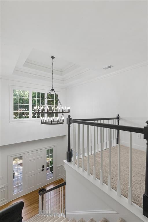 staircase featuring a chandelier, wood-type flooring, a raised ceiling, and plenty of natural light