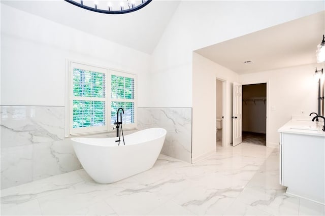 bathroom featuring vaulted ceiling, a bathtub, vanity, and tile walls