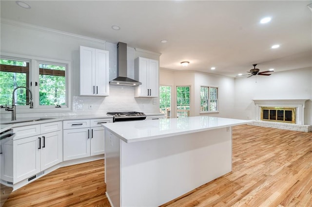 kitchen with white cabinetry, a center island, sink, wall chimney range hood, and stainless steel stove