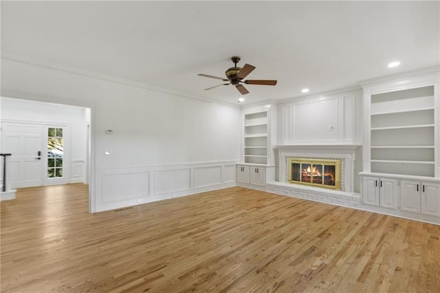 unfurnished living room featuring built in shelves, ceiling fan, light hardwood / wood-style floors, and a brick fireplace