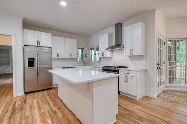 kitchen with stainless steel appliances, white cabinetry, plenty of natural light, and wall chimney range hood