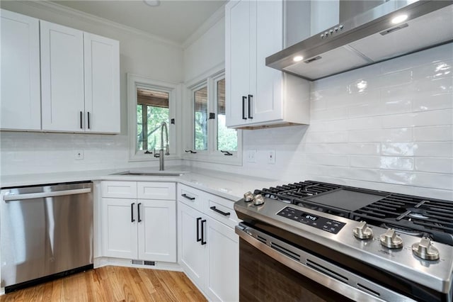 kitchen with light wood-type flooring, wall chimney exhaust hood, stainless steel appliances, sink, and white cabinets