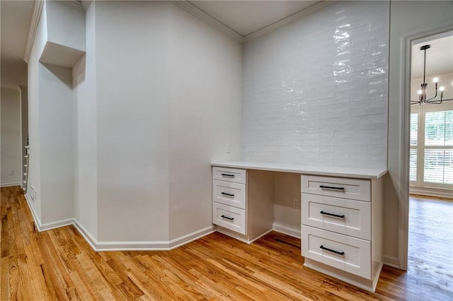 unfurnished office featuring light wood-type flooring, built in desk, crown molding, and a chandelier