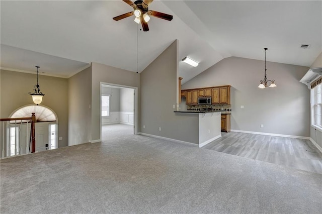 unfurnished living room with light carpet, ceiling fan with notable chandelier, and vaulted ceiling