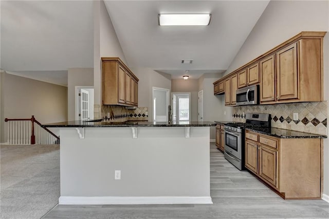 kitchen with a breakfast bar, kitchen peninsula, stainless steel appliances, and dark stone counters