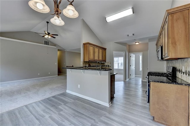 kitchen featuring kitchen peninsula, pendant lighting, dark stone countertops, black gas range, and lofted ceiling