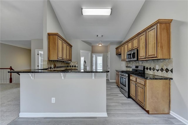 kitchen featuring stainless steel appliances, tasteful backsplash, kitchen peninsula, dark stone countertops, and a breakfast bar area