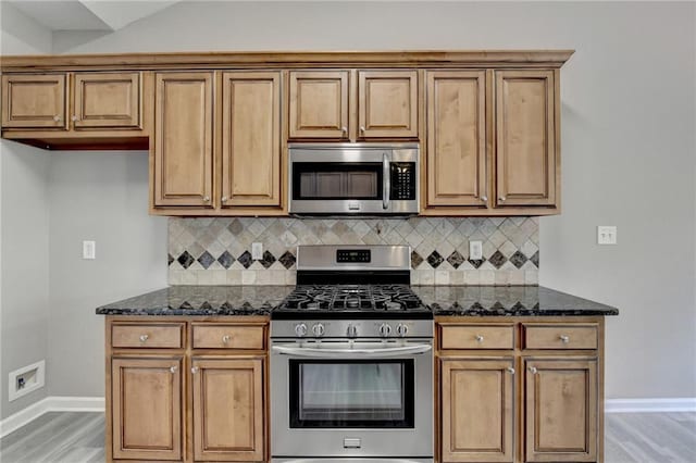 kitchen with backsplash, light hardwood / wood-style floors, stainless steel appliances, and dark stone counters