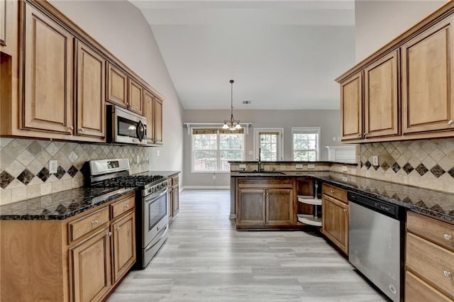 kitchen with lofted ceiling, dark stone counters, hanging light fixtures, light hardwood / wood-style flooring, and stainless steel appliances