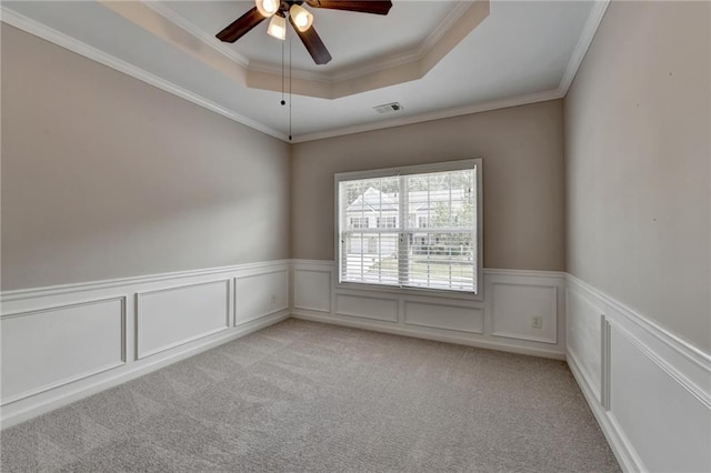 empty room featuring a raised ceiling, ceiling fan, crown molding, and light carpet