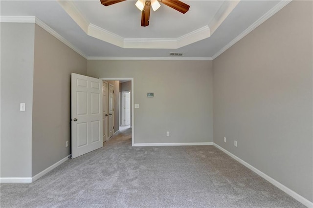 carpeted spare room with ceiling fan, crown molding, and a tray ceiling