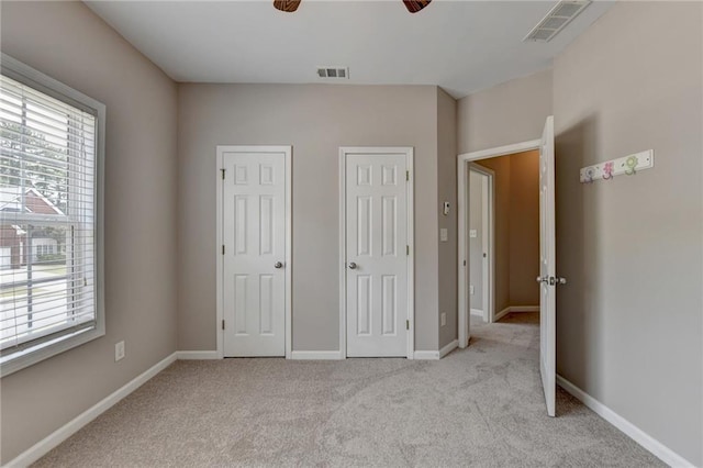 unfurnished bedroom with ceiling fan, light colored carpet, and two closets