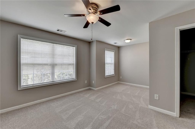 unfurnished bedroom featuring a spacious closet, a closet, ceiling fan, and light colored carpet