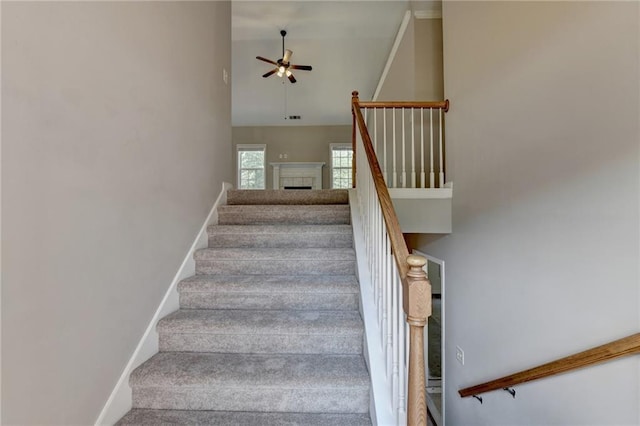 stairway featuring ceiling fan, a tile fireplace, carpet floors, and a high ceiling