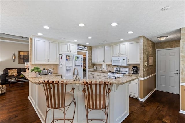 kitchen featuring white appliances, a peninsula, dark wood-style flooring, white cabinets, and a breakfast bar area