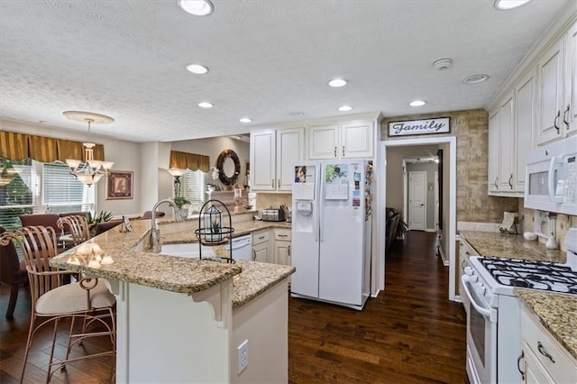 kitchen featuring white appliances, a textured ceiling, a breakfast bar area, a sink, and dark wood finished floors