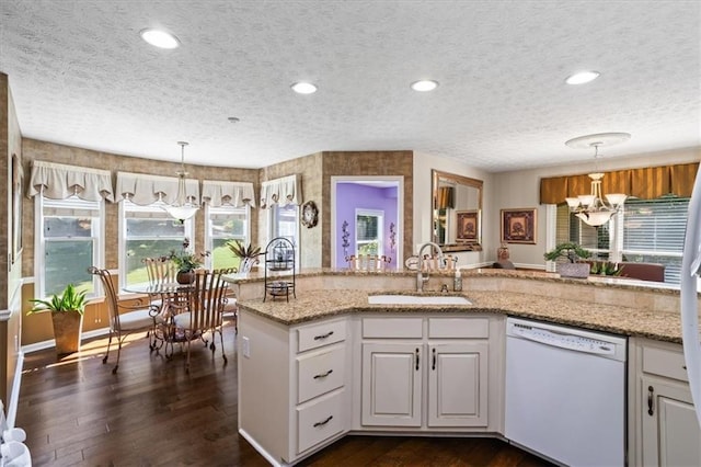 kitchen with white dishwasher, a sink, a chandelier, a textured ceiling, and dark wood-type flooring
