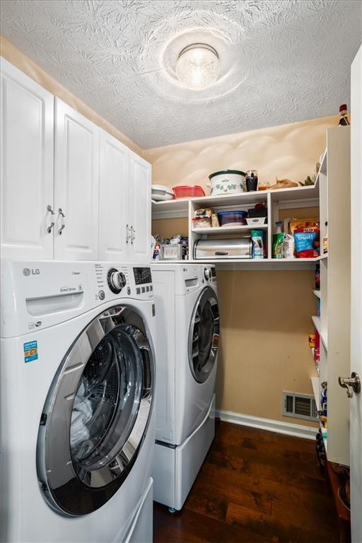 washroom featuring cabinet space, washer and dryer, dark wood finished floors, and a textured ceiling