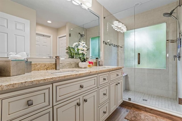 full bath with a stall shower, double vanity, and wood finished floors