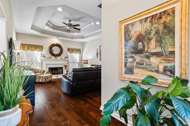 living area with ceiling fan, hardwood / wood-style flooring, a tray ceiling, a high end fireplace, and recessed lighting