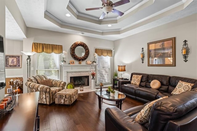living area featuring plenty of natural light, crown molding, a ceiling fan, a premium fireplace, and a tray ceiling