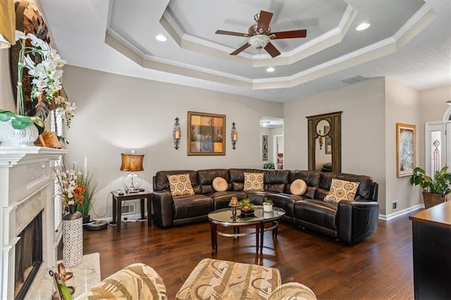 living room with ceiling fan, crown molding, a tray ceiling, wood finished floors, and a premium fireplace
