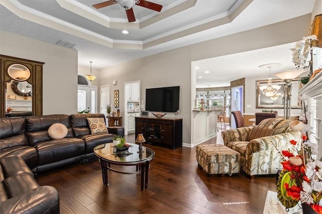 living area with a ceiling fan, dark wood-style flooring, a raised ceiling, crown molding, and a chandelier