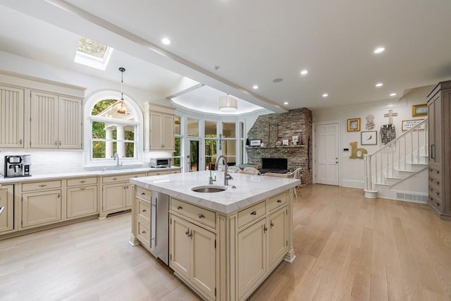 kitchen featuring a skylight, a brick fireplace, open floor plan, light wood-style flooring, and cream cabinetry
