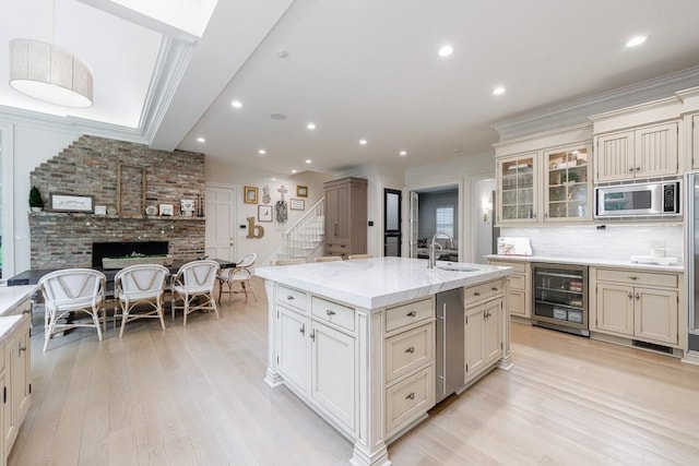 kitchen featuring a sink, stainless steel microwave, light wood-type flooring, and beverage cooler