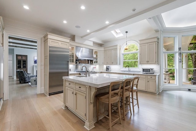 kitchen with cream cabinetry, tasteful backsplash, wall chimney range hood, and stainless steel built in refrigerator