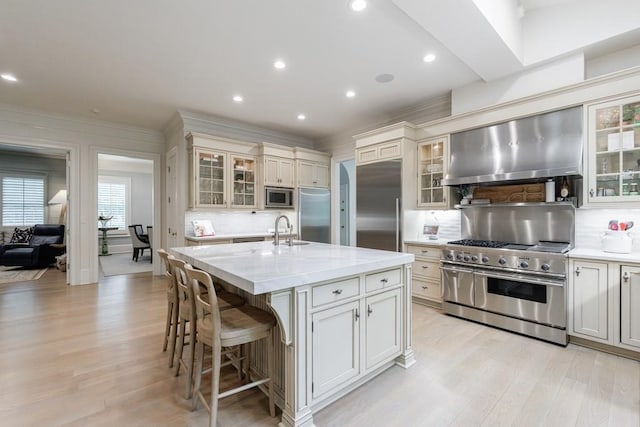 kitchen with ornamental molding, built in appliances, light wood-style floors, wall chimney range hood, and tasteful backsplash