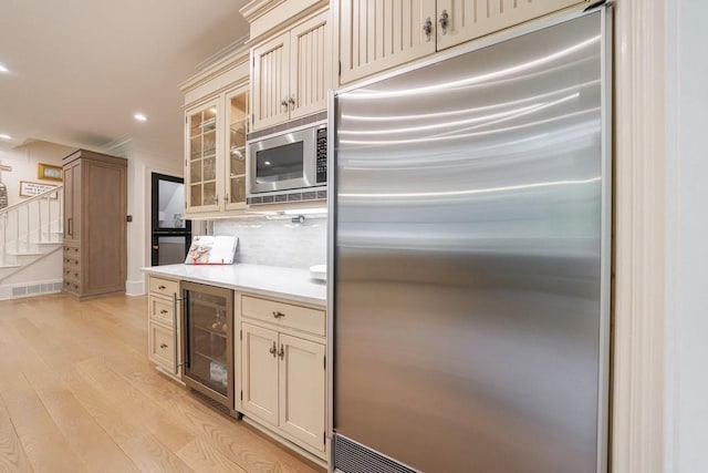 kitchen featuring built in appliances, wine cooler, light wood-style floors, light countertops, and cream cabinetry