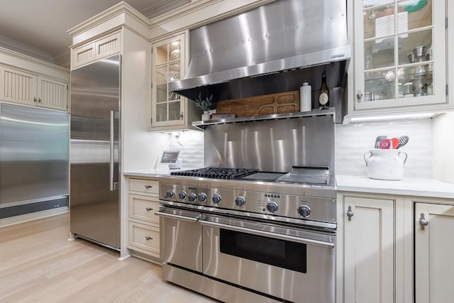 kitchen featuring extractor fan, light countertops, light wood-style flooring, backsplash, and premium appliances