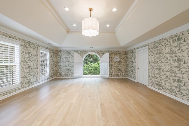 unfurnished room featuring crown molding, a chandelier, light wood-style floors, a tray ceiling, and wallpapered walls