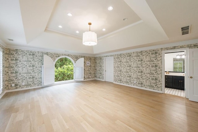 unfurnished living room featuring visible vents, ornamental molding, light wood-style floors, wallpapered walls, and a raised ceiling