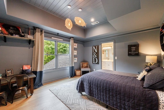 bedroom featuring visible vents, light wood-style floors, wood ceiling, a tray ceiling, and ensuite bath