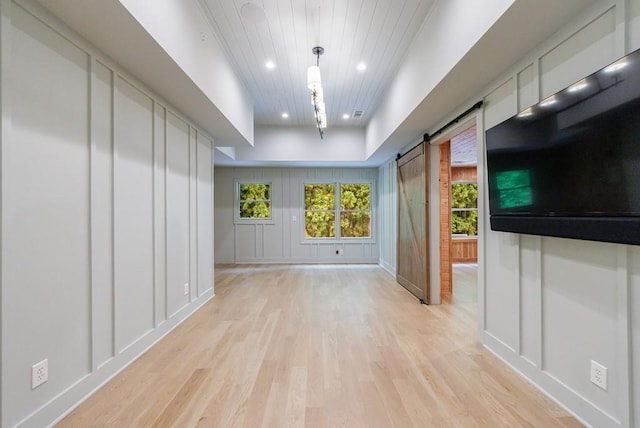unfurnished living room featuring a decorative wall, light wood-style floors, recessed lighting, a barn door, and wood ceiling