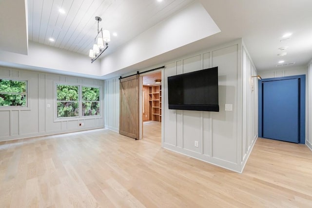unfurnished living room with a decorative wall, light wood finished floors, a barn door, and visible vents