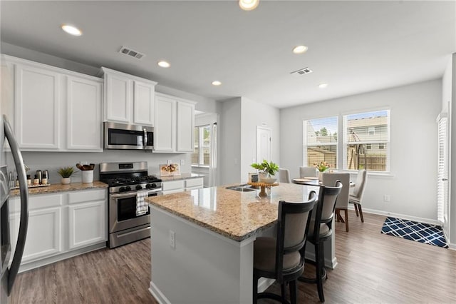 34 Hemlock Gln, Dallas, GA 30132 - kitchen with stainless steel appliances, an island with sink, dark wood-style flooring, white cabinets, and plenty of natural light