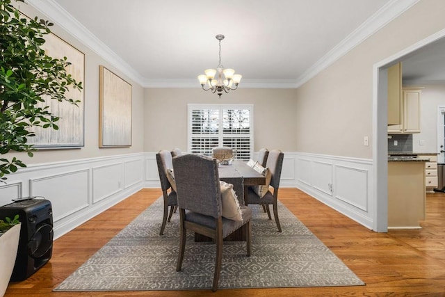 dining room with an inviting chandelier, light wood-style flooring, a decorative wall, and crown molding