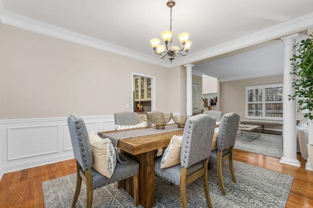 dining area featuring wood finished floors, a wainscoted wall, decorative columns, ornamental molding, and a notable chandelier