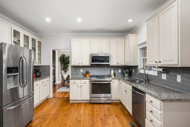 kitchen featuring light wood-type flooring, a sink, tasteful backsplash, stainless steel appliances, and glass insert cabinets