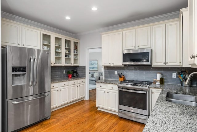 kitchen with light wood-style flooring, a sink, glass insert cabinets, appliances with stainless steel finishes, and backsplash