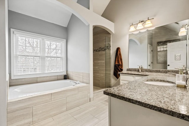 bathroom with tiled shower, a garden tub, lofted ceiling, and vanity