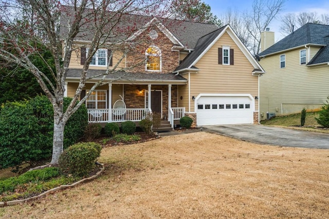 traditional-style house with aphalt driveway, stone siding, covered porch, an attached garage, and a shingled roof