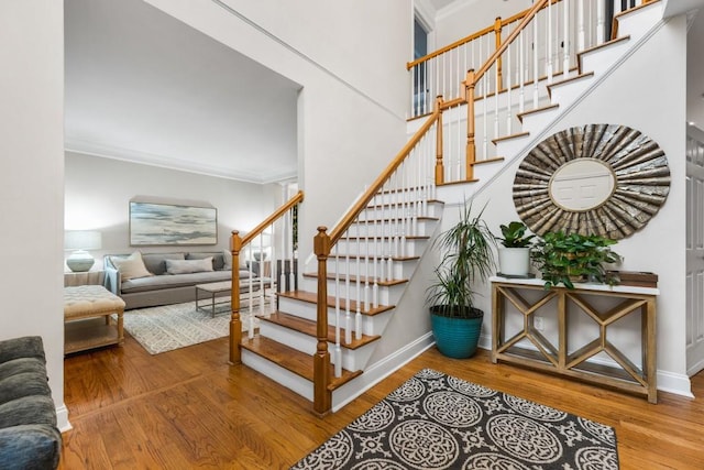 stairway with wood finished floors, baseboards, a towering ceiling, and ornamental molding