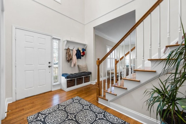 foyer with wood finished floors, baseboards, a high ceiling, stairs, and crown molding