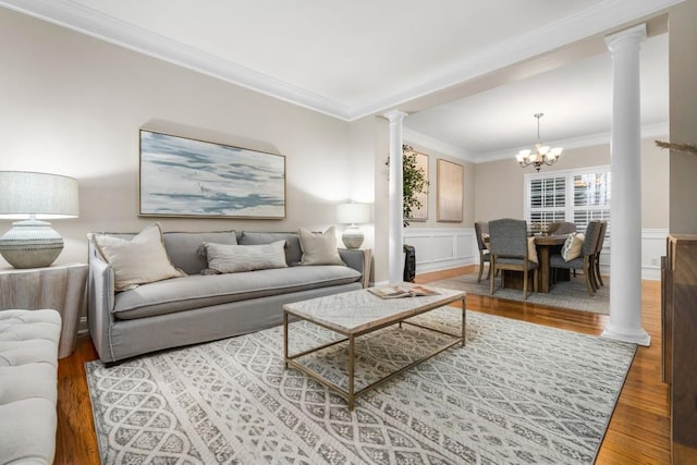 living area with a wainscoted wall, wood finished floors, crown molding, and decorative columns