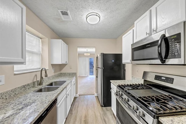 kitchen with white cabinets, appliances with stainless steel finishes, light wood-type flooring, and a textured ceiling