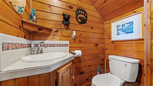 bathroom with toilet, vanity, vaulted ceiling, and wooden walls